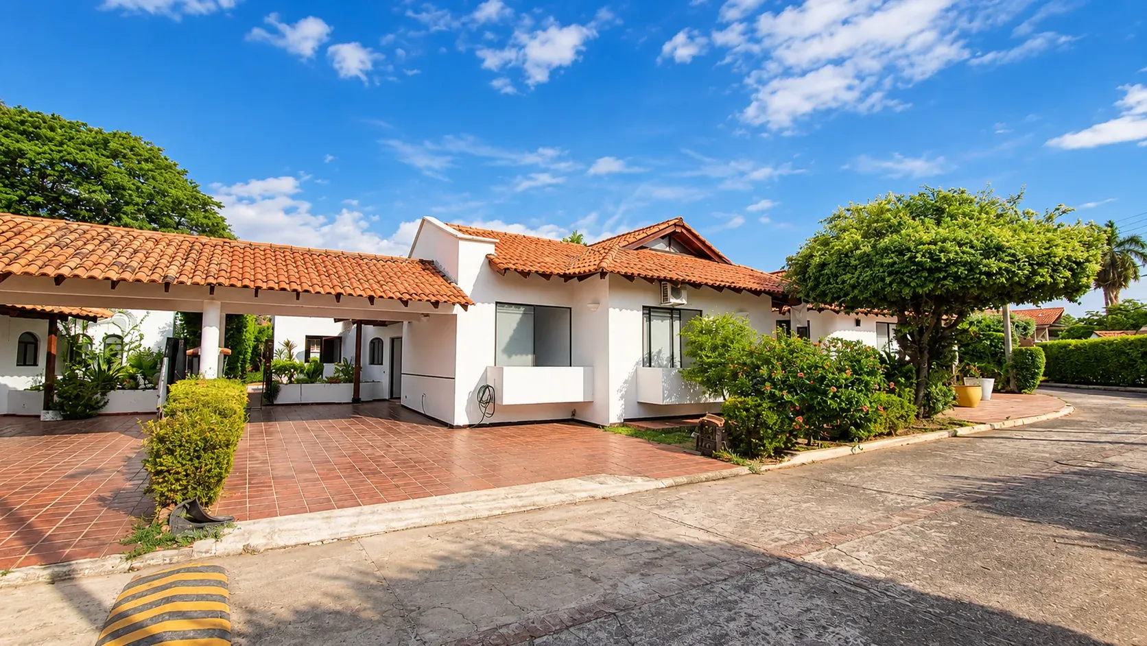 Fachada de la casa con techo de teja y garaje cubierto, sobre una calle interna del condominio