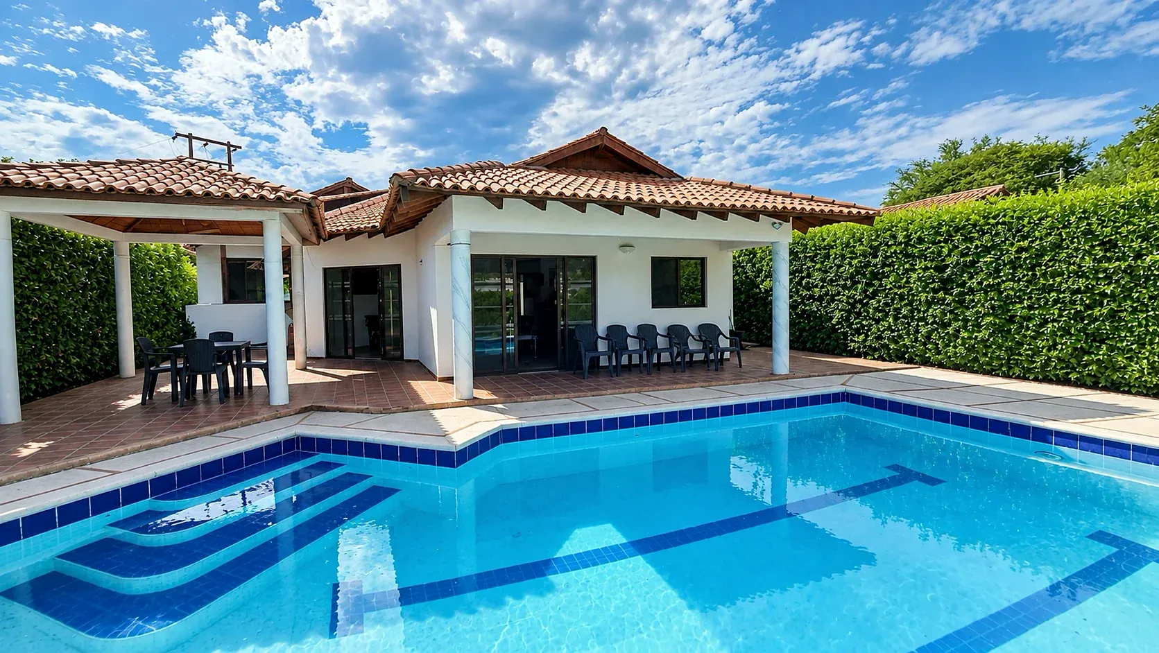 Casa de una planta con techo de teja frente a la piscina privada, rodeada de setos altos